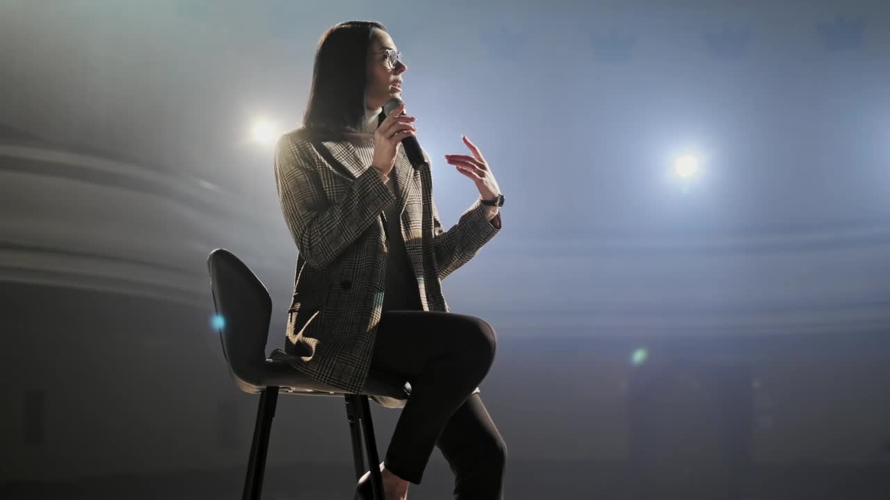 Stock Video Female Speaker Speaks To Audience Sitting On A Chair Live Wallpaper For PC