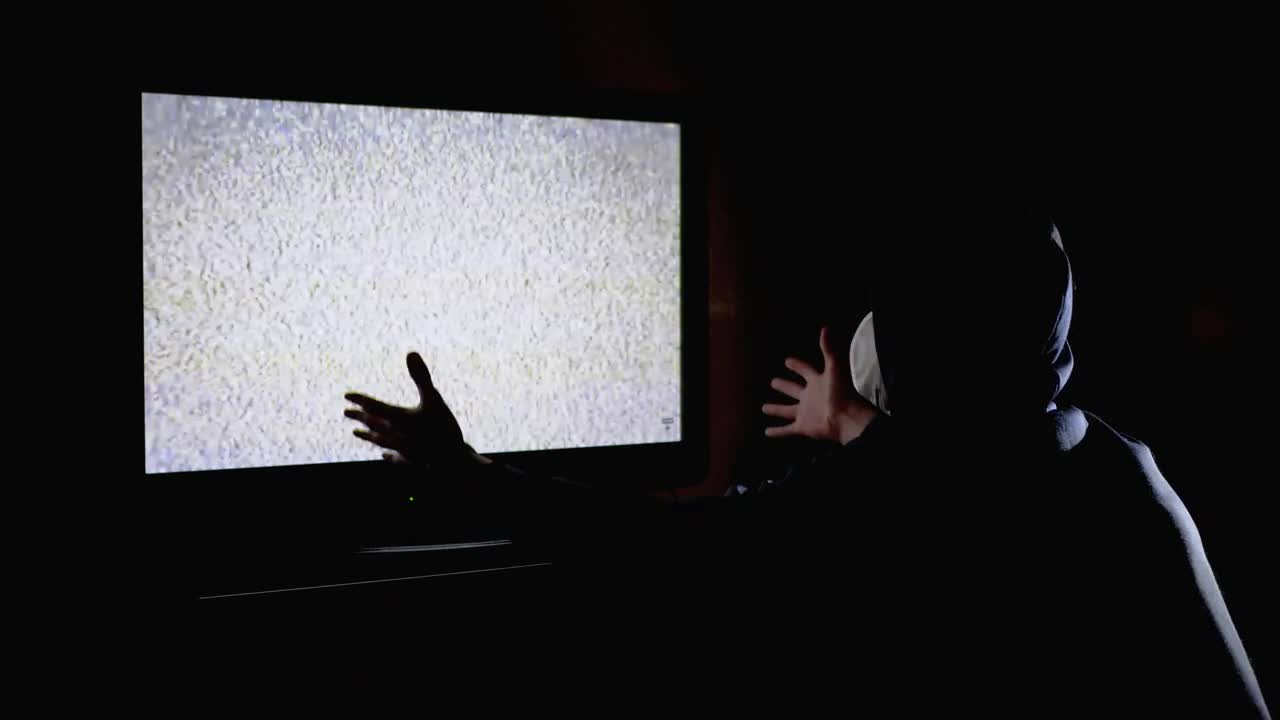 Stock Video Man In A Hoodie In Front Of A Tv With Animated Wallpaper