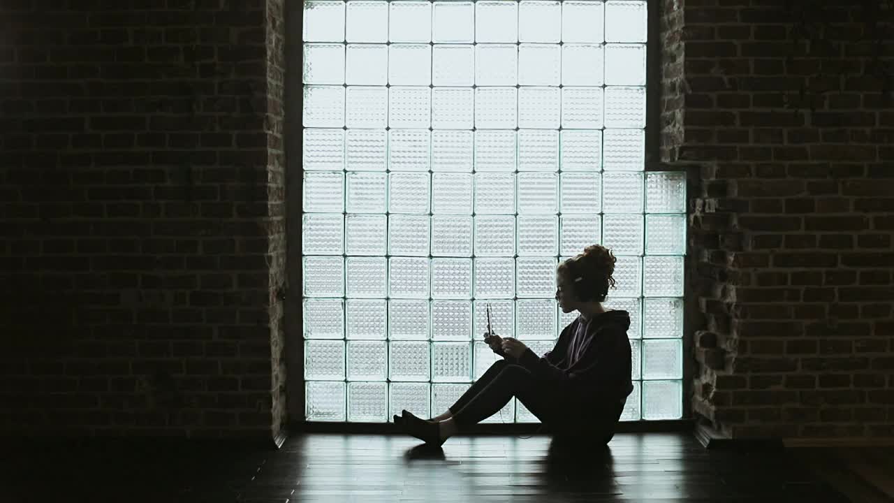Stock Video Lonley Girl Sitting On Floor With Headphones Backlit By Window Animated Wallpaper