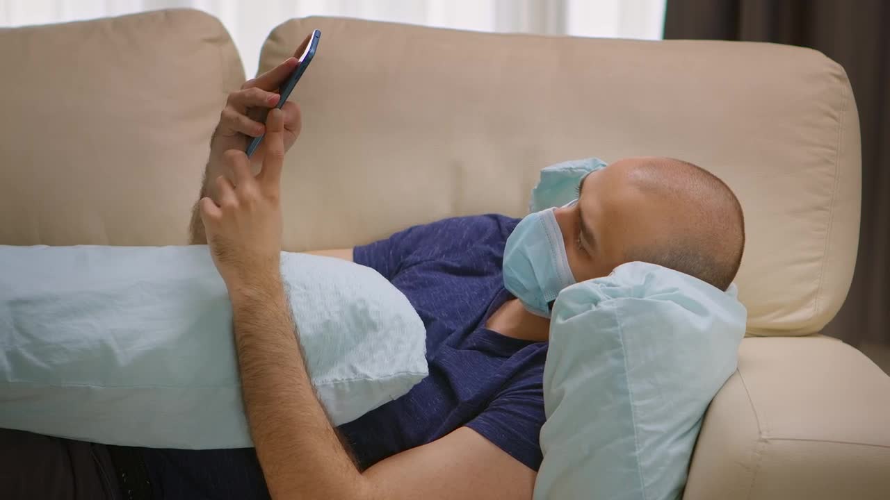 Stock Video Man With Covid Lays On Sofa With Mobile Phon Animated Wallpaper