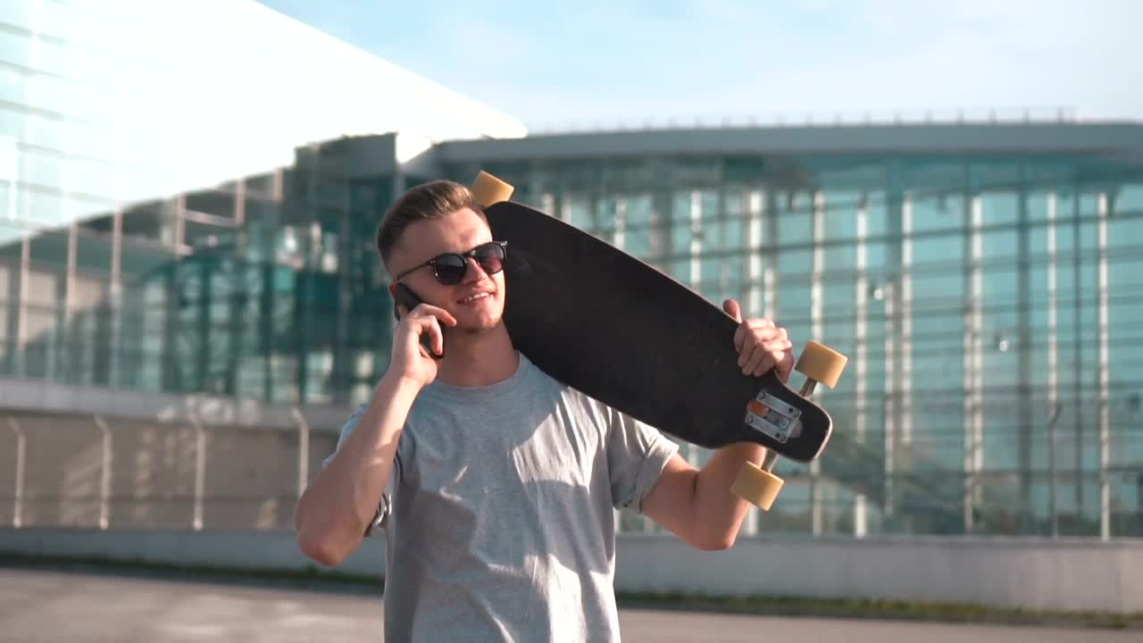 Stock Video Man Talking On The Phone Carrying A Longboar Animated Wallpaper