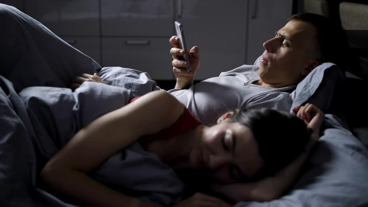 Stock Video Man Using His Phone While His Wife Sleep Animated Wallpaper